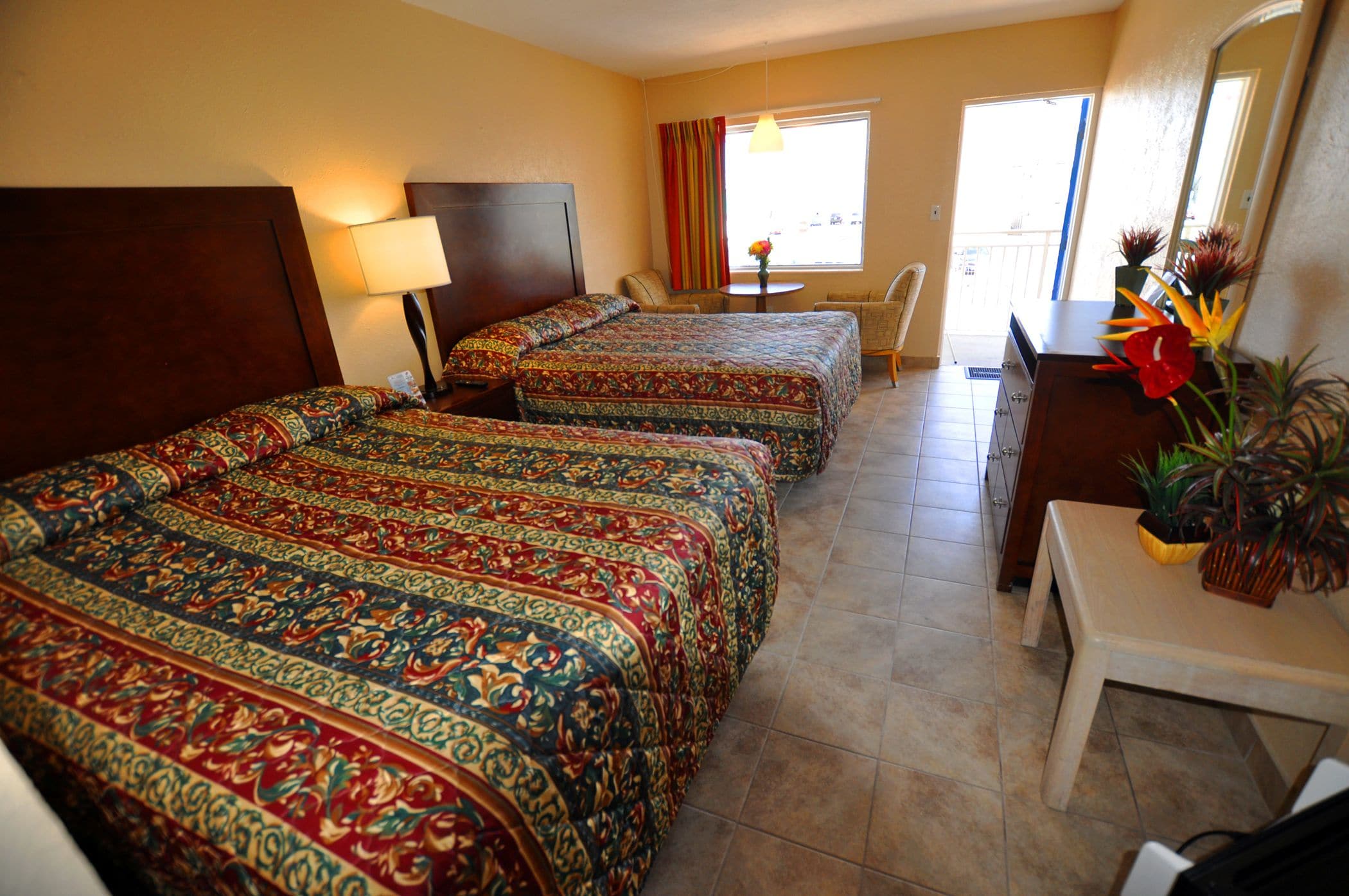 A hotel room with two beds, a desk, a chair, a small table, and a window with curtains.