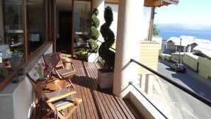 A balcony with wooden furniture, a potted plant, and a view of the sea and buildings. - View Hotel BRC (San Carlos de Bariloche)