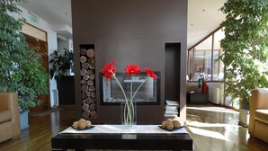 A modern living room with a dark wooden coffee table, two vases with red flowers, and a fireplace. - View Hotel BRC (San Carlos de Bariloche)