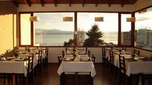 A dining area with tables set for service, large windows offering a view of a body of water and distant mountains, and pendant lighting. - View Hotel BRC (San Carlos de Bariloche)
