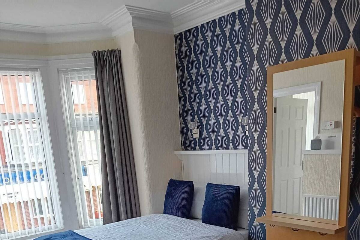A bedroom with a bed, a dresser, a mirror, and a patterned wall.