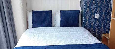 Una cama con cabecera de estampado blanco y azul, dos almohadas azules y una colcha azul oscuro.