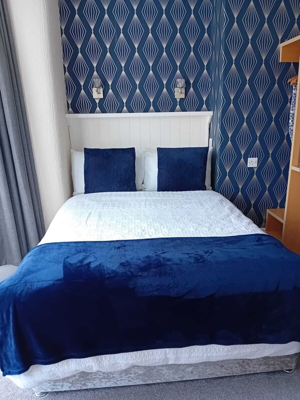 Una cama con cabecera de estampado blanco y azul, dos almohadas azules y una colcha azul oscuro.