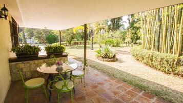 A patio with a round table and four chairs, surrounded by a garden with various plants and a bamboo fence.