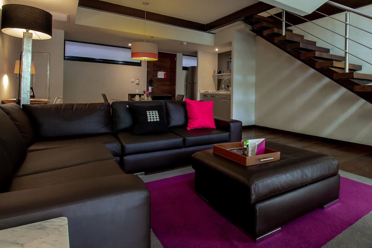 Ein modernes Wohnzimmer mit einem Ecksofa, einem Couchtisch, einer Treppe und einer Küche im Hintergrund.
