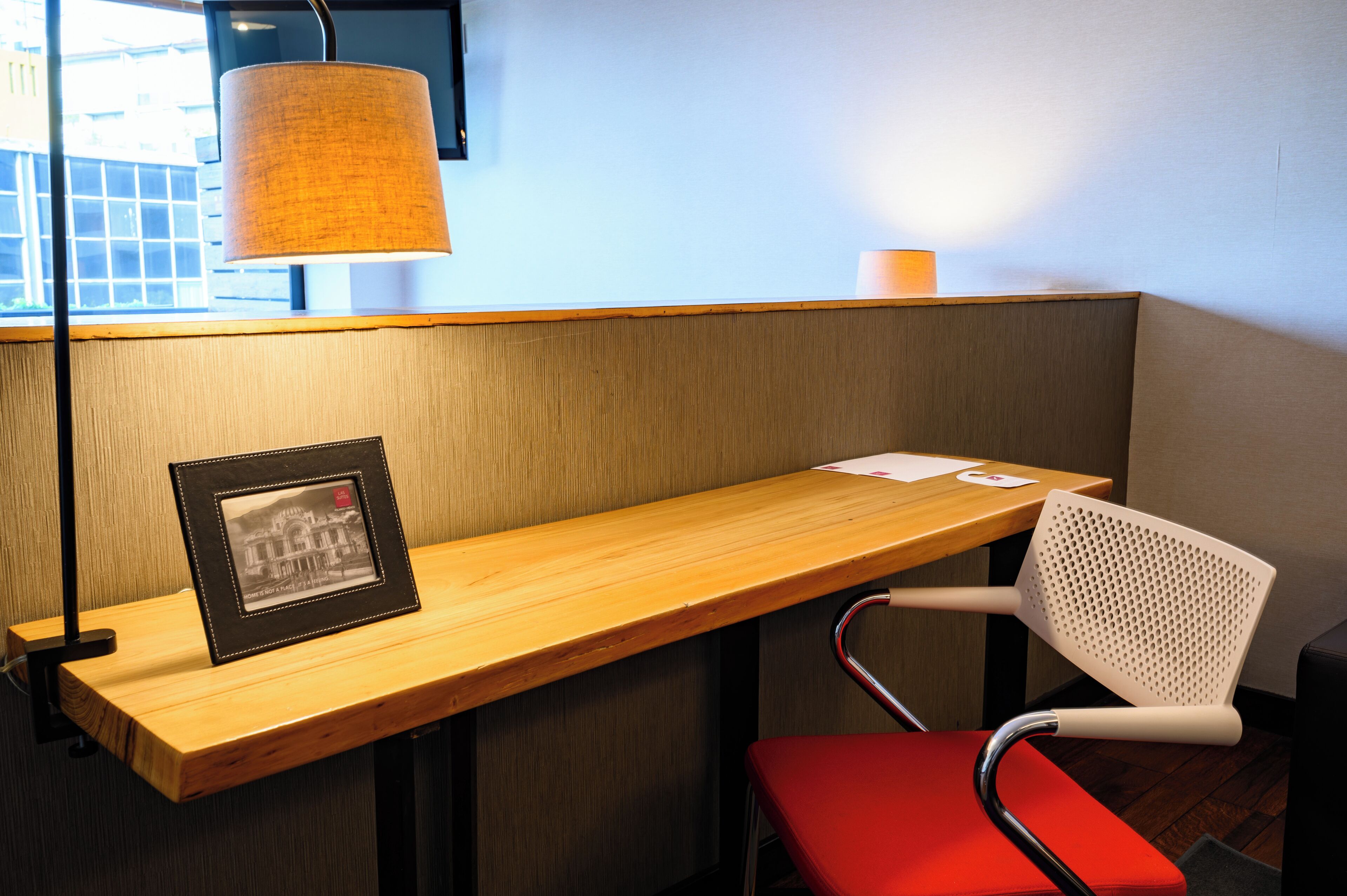 A corner seating area with a wooden bench, a red chair, a framed picture, and a lamp.