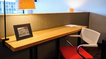 A corner seating area with a wooden bench, a red chair, a framed picture, and a lamp.