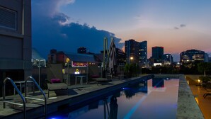 Piscina en la azotea con vista al horizonte de la ciudad, zona de bar con asientos y cielo despejado.