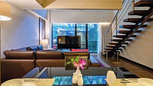 A modern living room with a sofa, a dining table set for two, and a staircase.