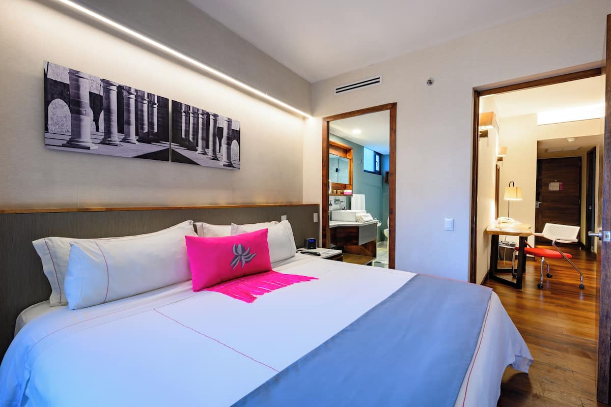 Ein Hotelzimmer mit einem großen Bett, einem Nachttisch, einem Spiegel und einem Bild an der Wand.