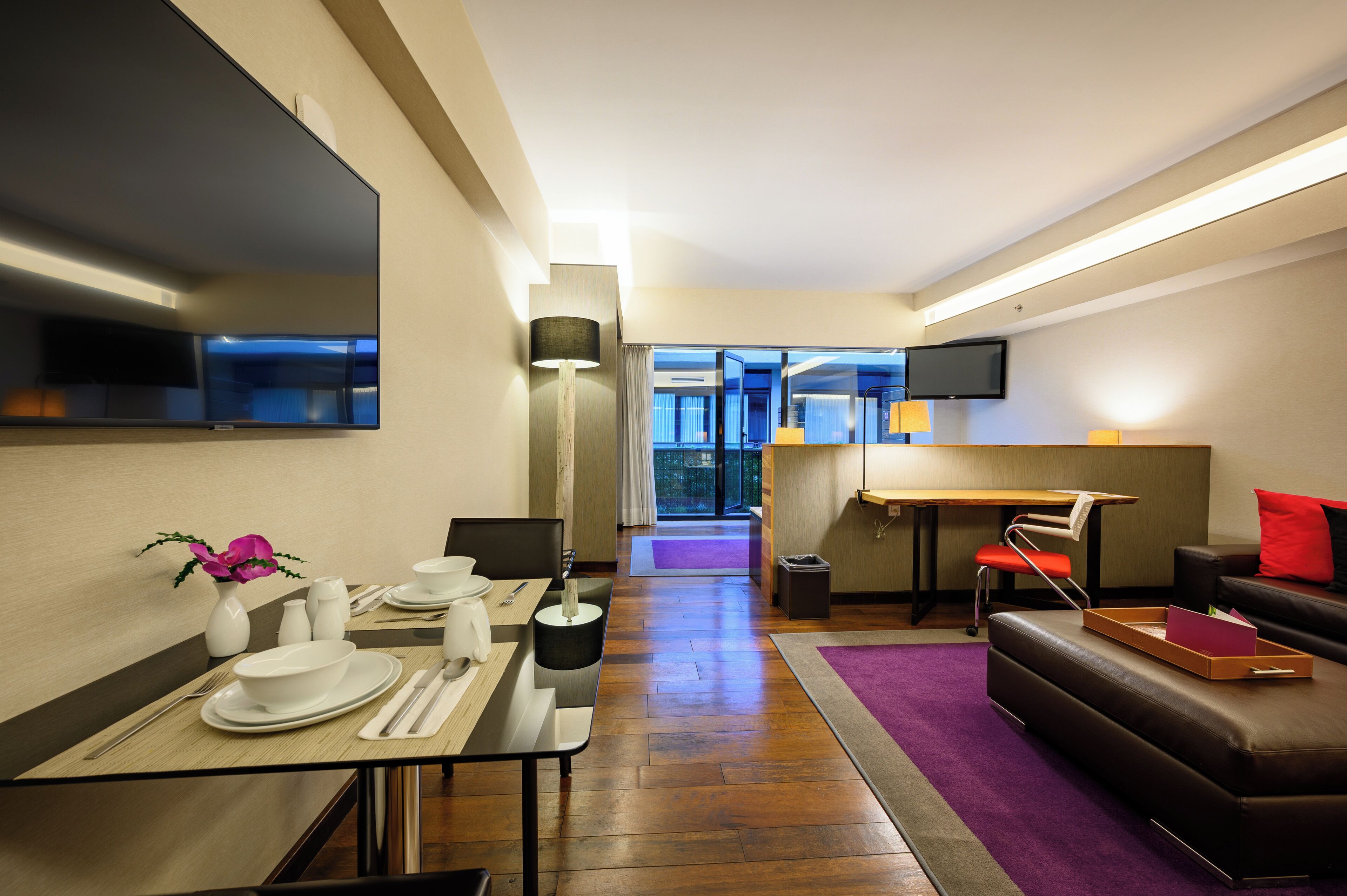 Ett modernt hotellrum med en matplats, en soffa, en TV och utsikt över staden.