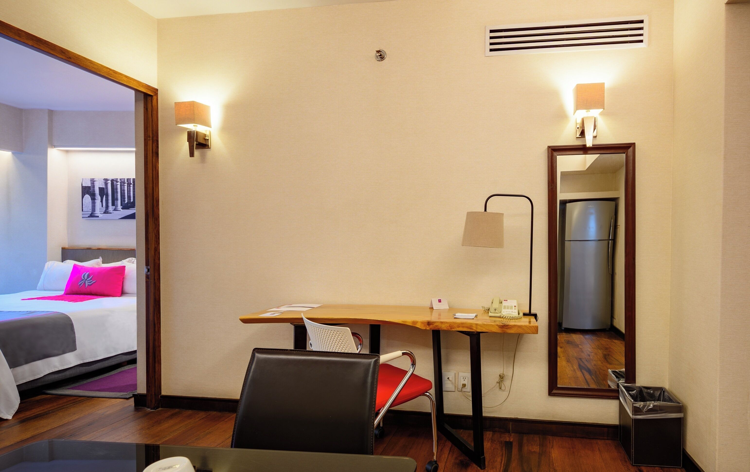 Hotelkamer met een bed, een bureau, een stoel, een spiegel, een koelkast en een prullenbak.