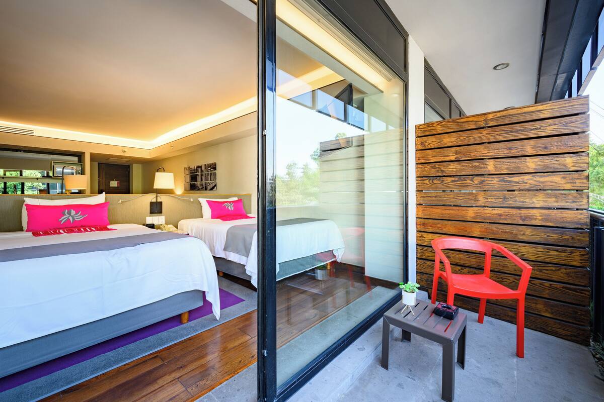 Ein modernes Hotelzimmer mit einem großen Bett, einem kleinen Tisch, einem roten Sessel und einem Balkon mit Holzverkleidung.