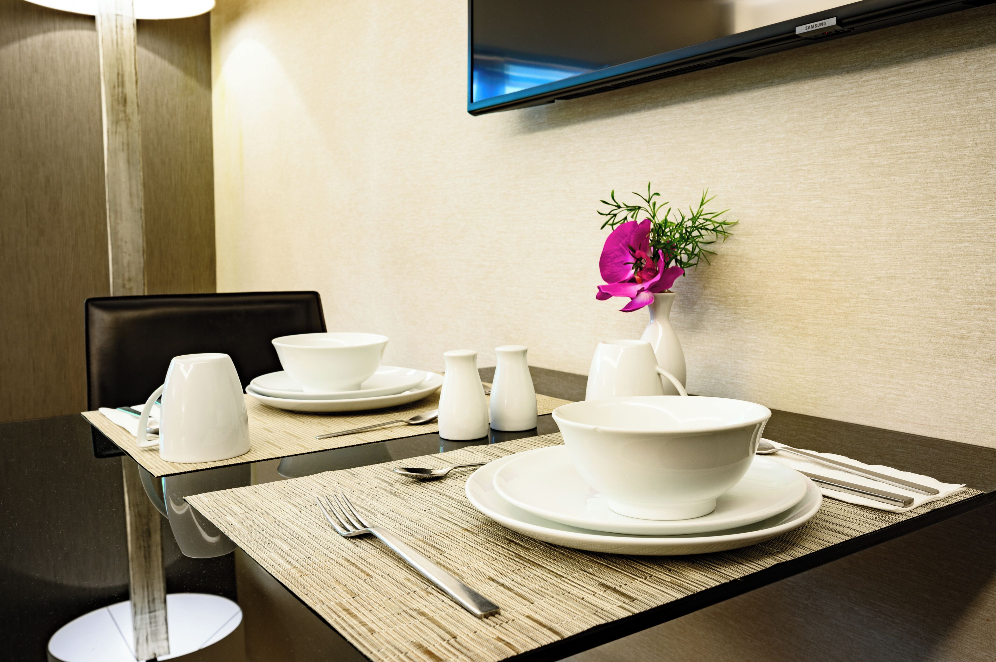 A dining table set with white plates, bowls, and cups, with a flower vase and salt shakers on the table.
