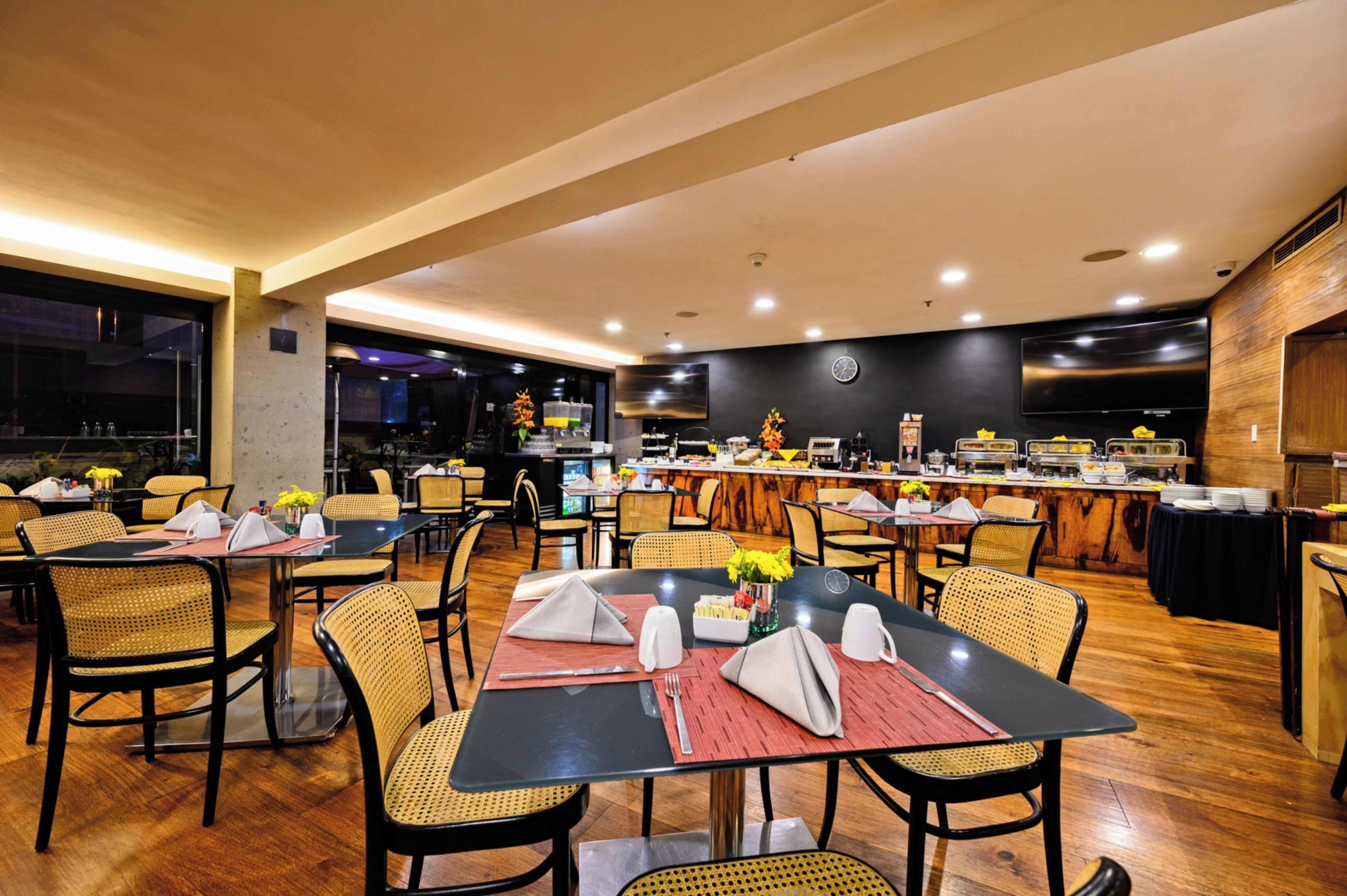 Un restaurante con varias mesas y sillas, una zona de bufé y un televisor colgado en la pared.
