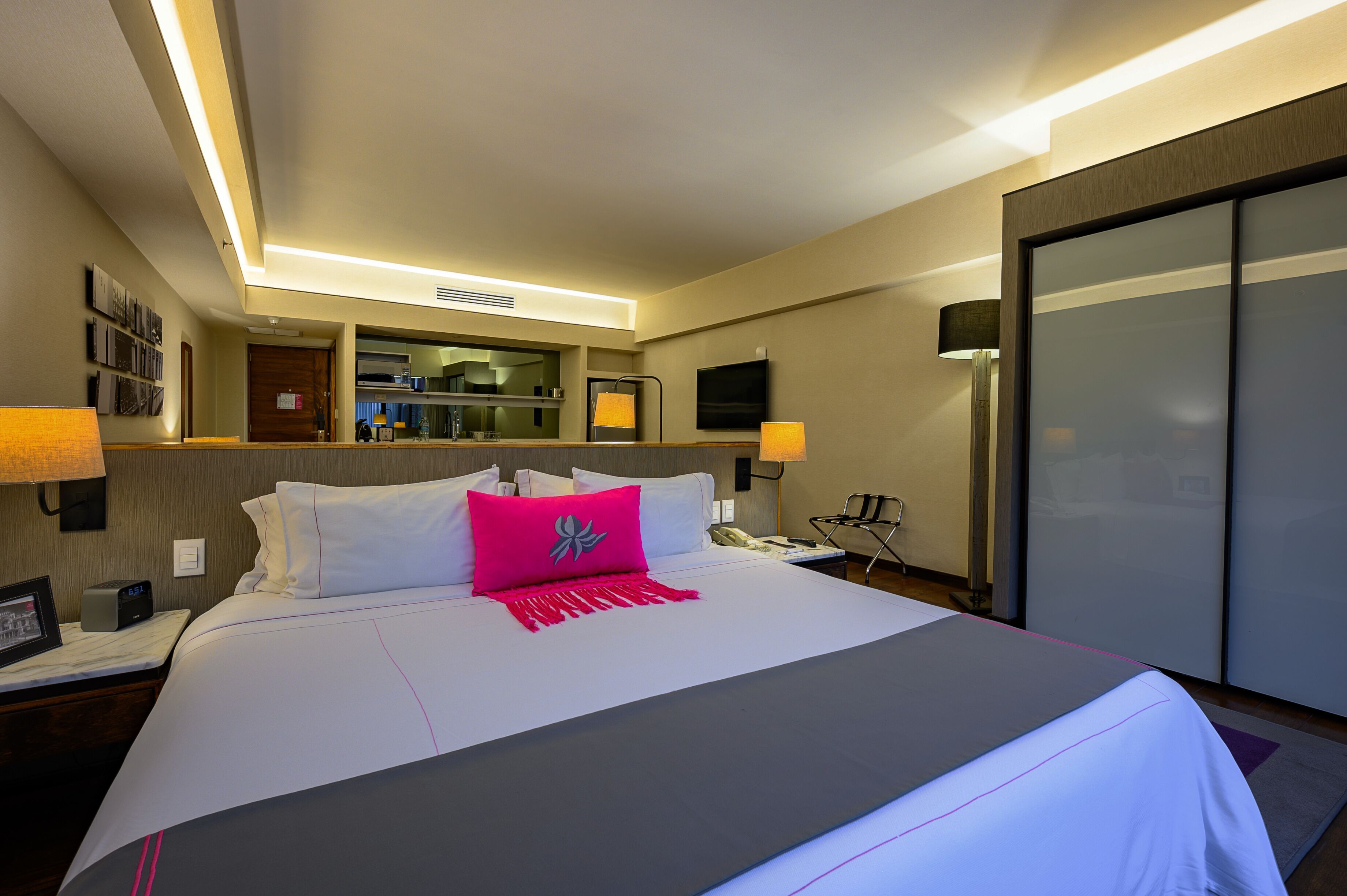 A hotel room with a large bed, bedside lamps, a flat-screen TV, a mirror, and a wardrobe.