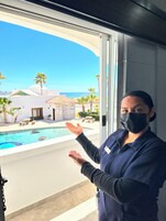 A person standing by a window overlooking a pool area with a view of a building and palm trees.