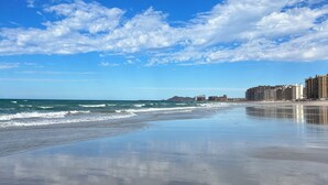 Una playa con cielo despejado y olas. Se ven edificios al fondo.