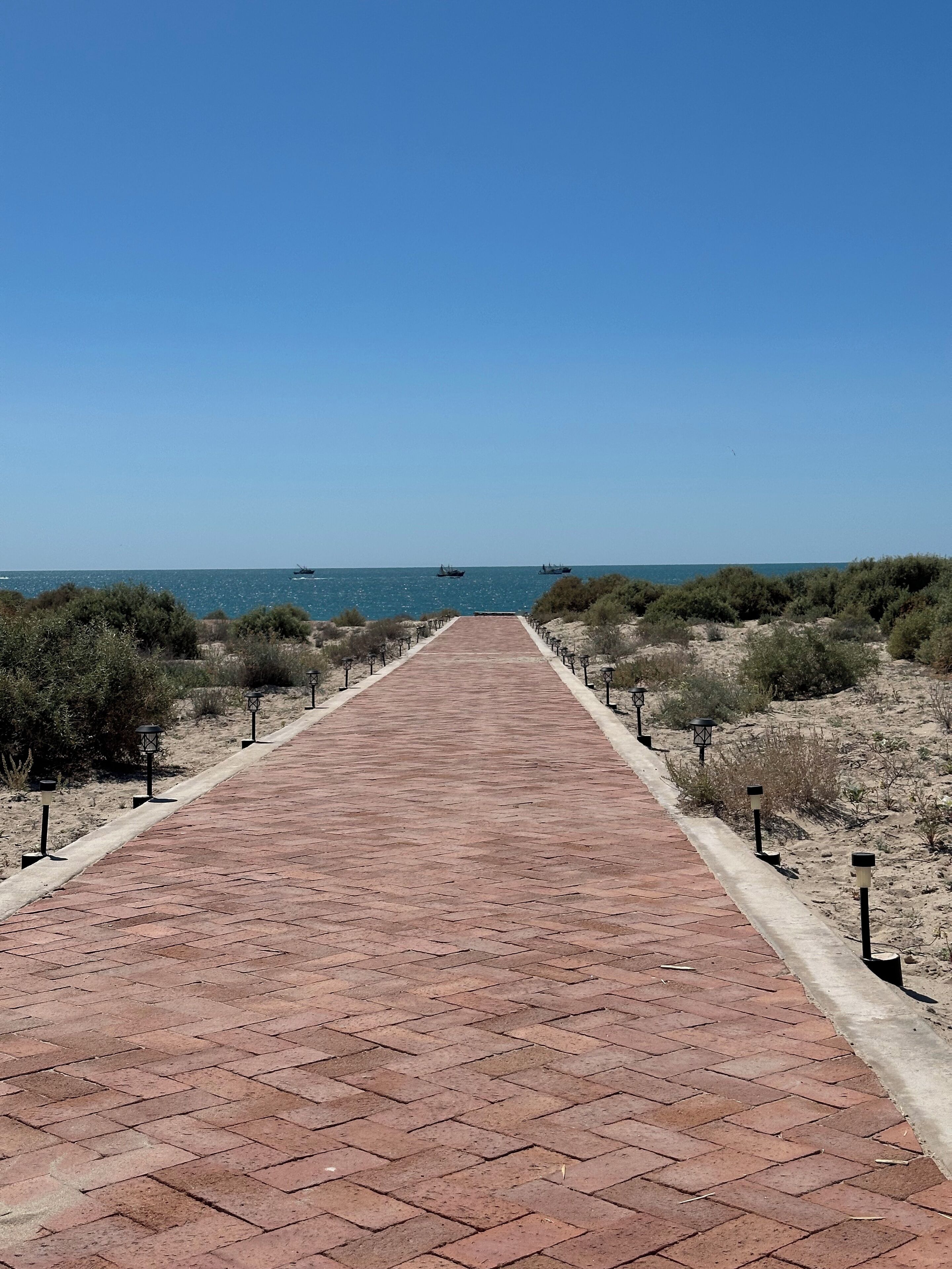 A paved pathway leading to a beach with a clear blue sky.
