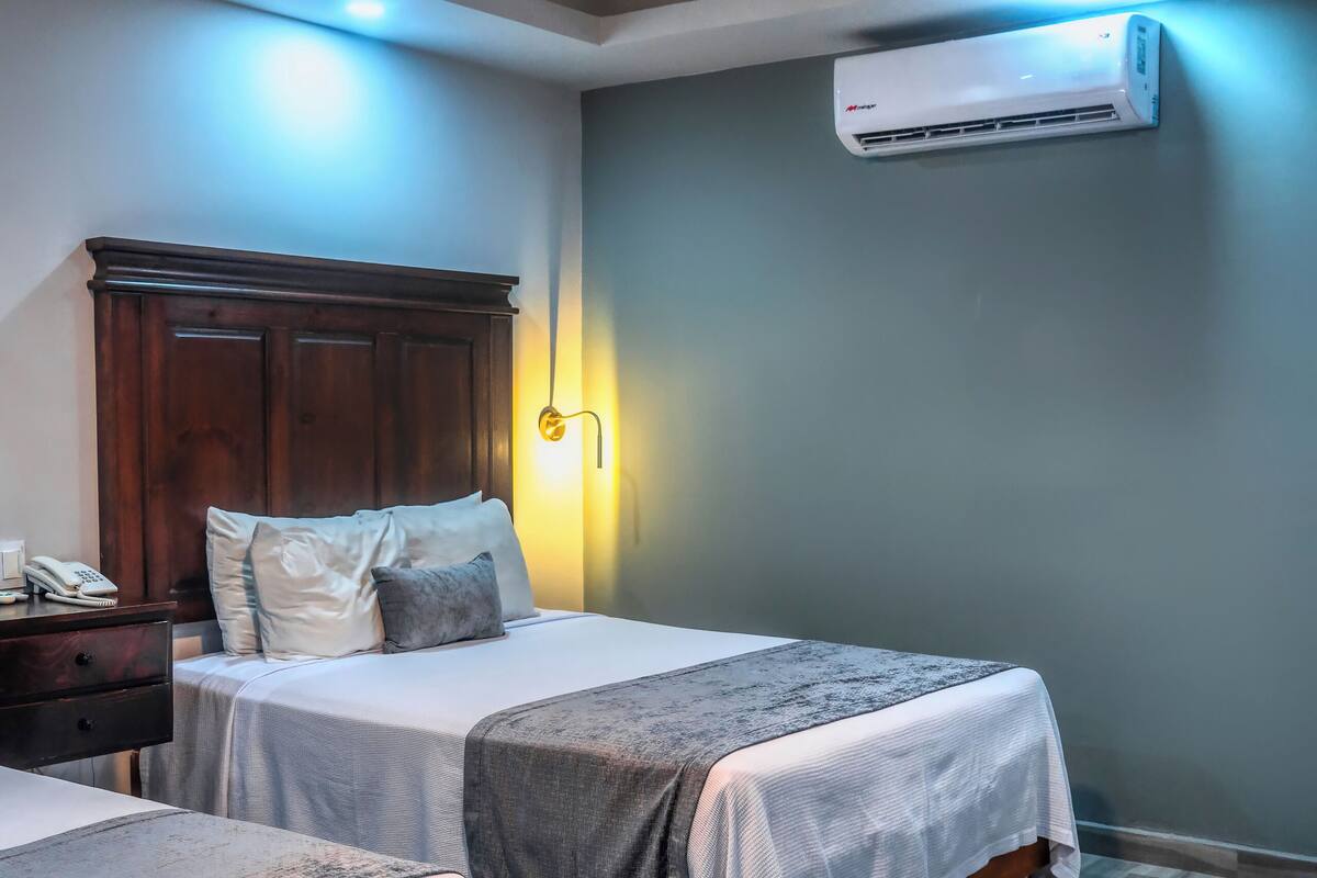 Une chambre d’hôtel avec deux lits, une tête de lit en bois, un ventilateur de plafond, un appareil de climatisation et une table de chevet avec un téléphone.
