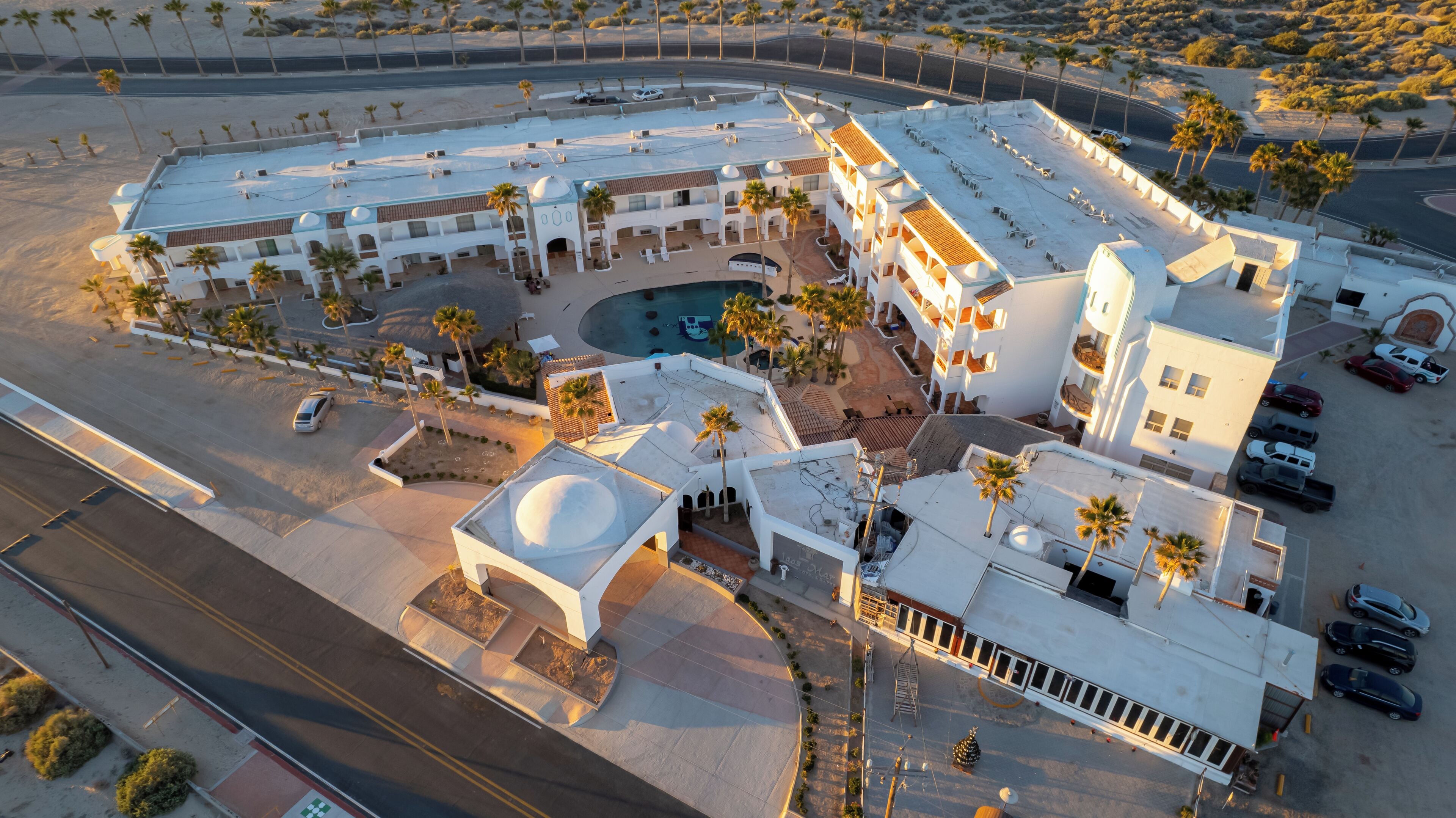 An aerial view of a hotel with a pool, multiple buildings, and palm trees.