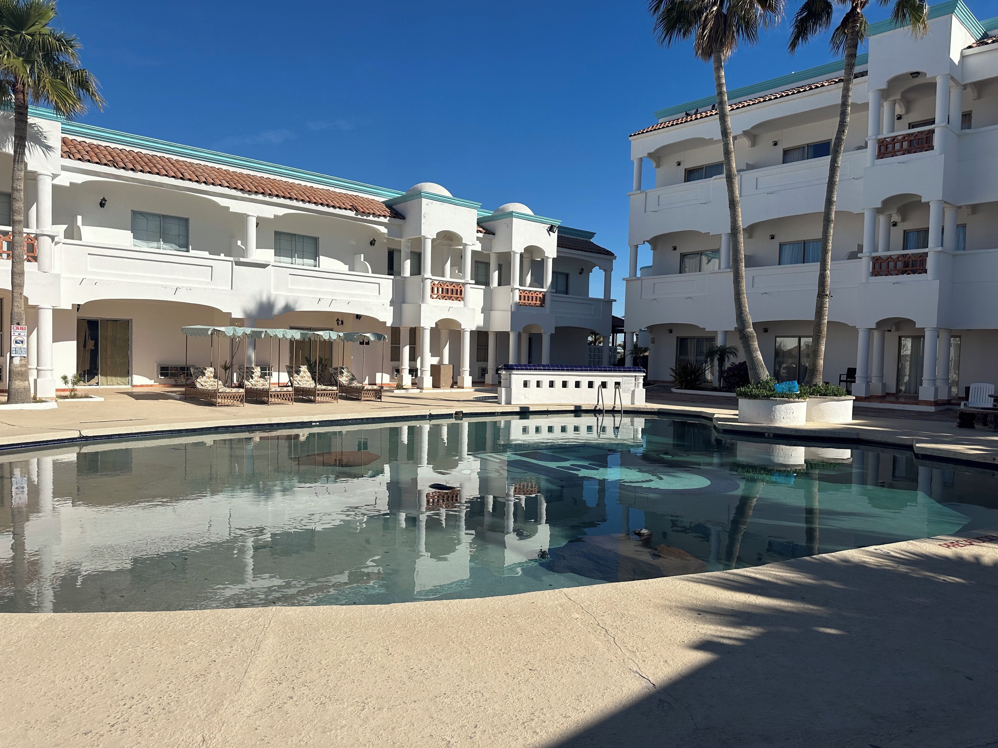 A resort with a swimming pool, palm trees, and a white building with balconies.