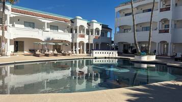 A resort with a swimming pool, palm trees, and a white building with balconies.