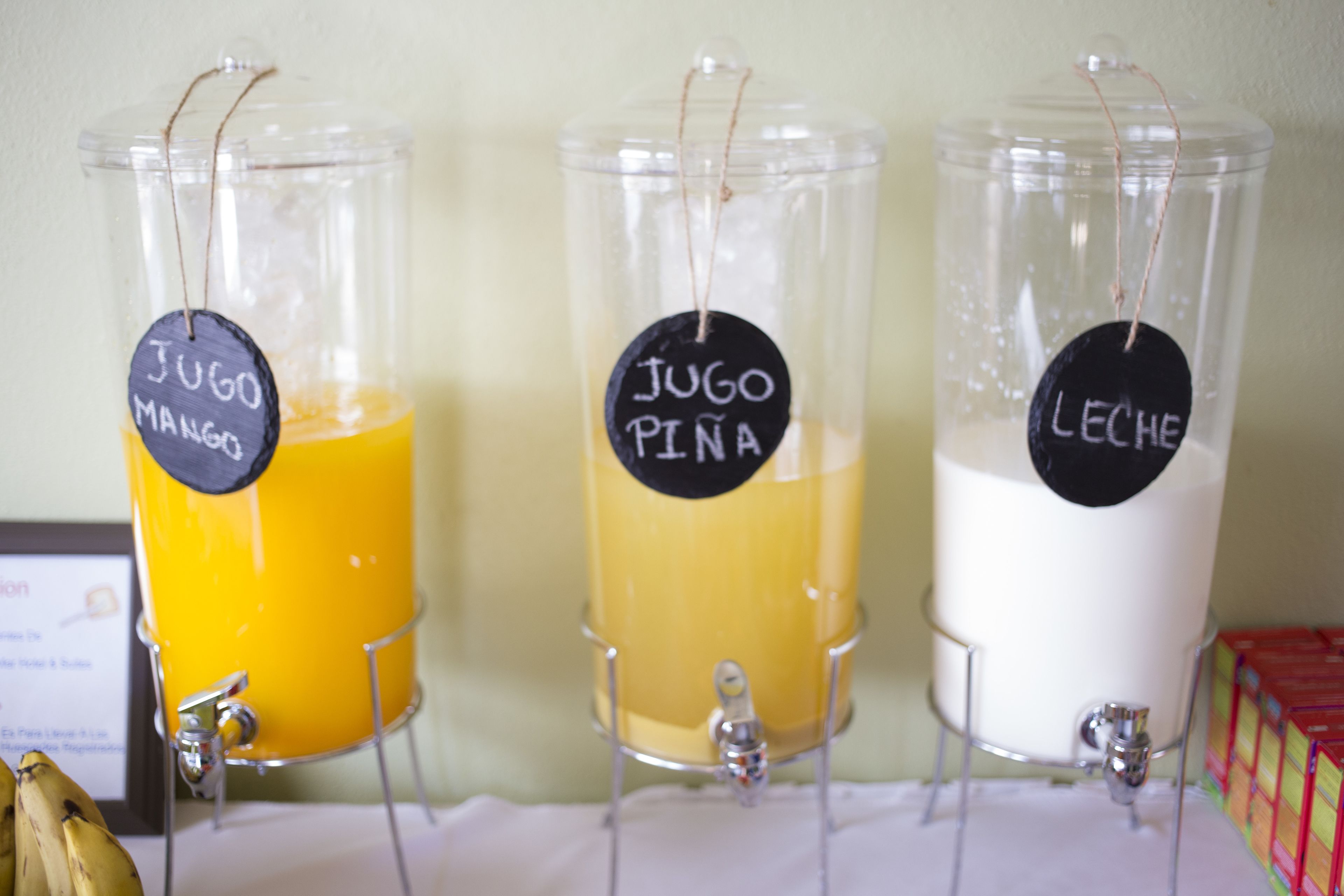 Three beverage dispensers labeled 'Jugo Mango,' 'Jugo Pina,' and 'Leche,' with a banana on the left.