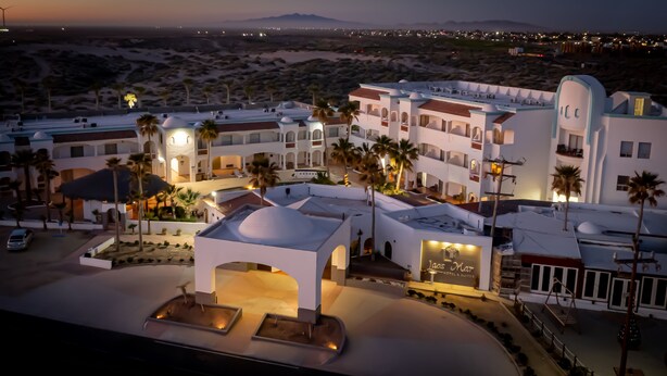 Un hotel con un patio central, palmeras y vistas al desierto y montañas al fondo.