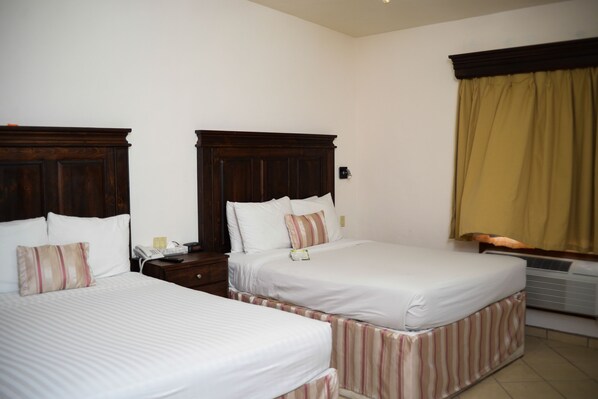 Habitación de hotel con dos camas individuales, una mesita de noche con teléfono y una ventana con cortinas.