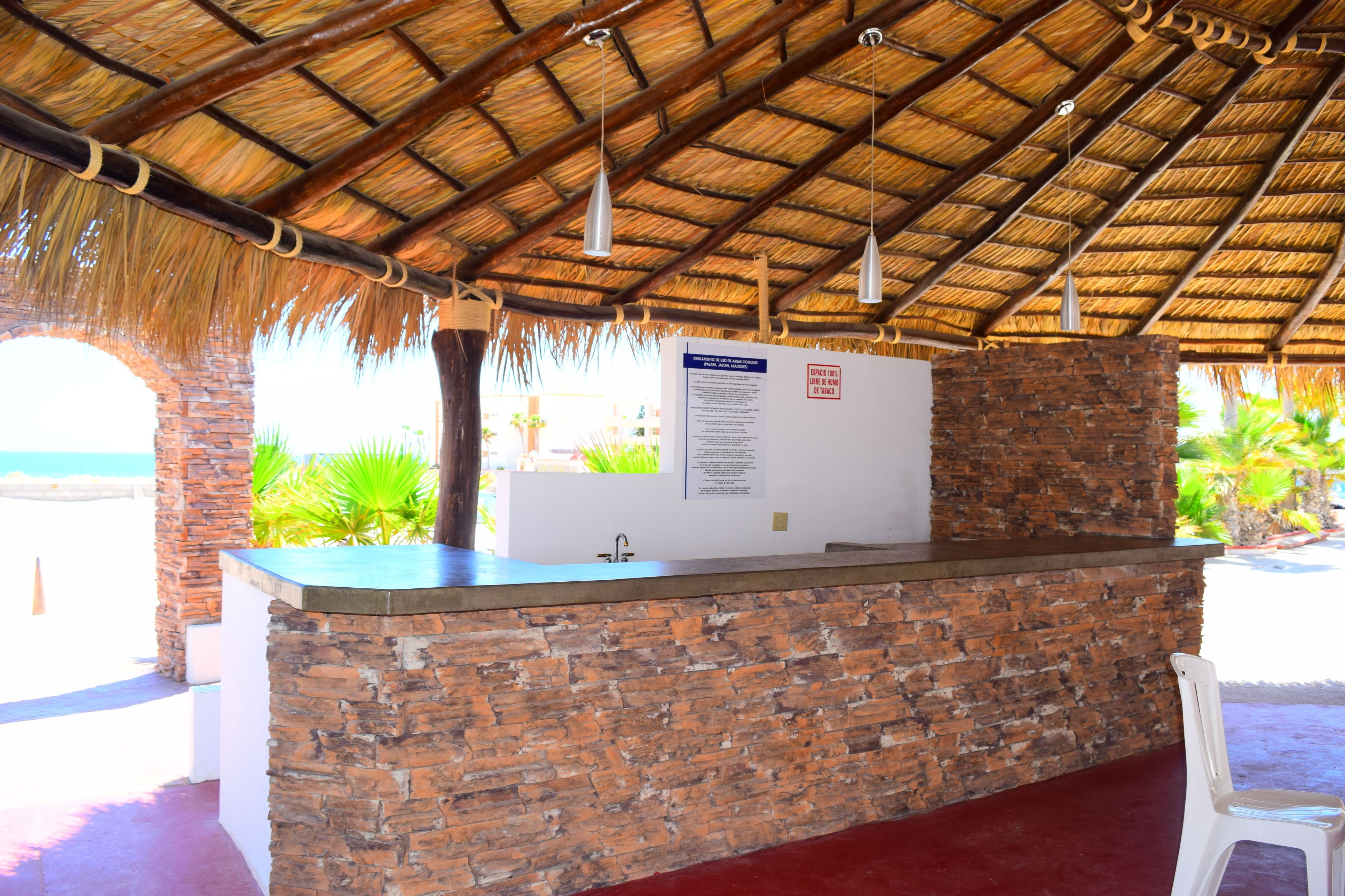 Una zona de recepción con mostrador de ladrillo, techo de paja y vista a la playa.