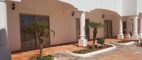 A courtyard with white walls, tiled flooring, and palm trees.