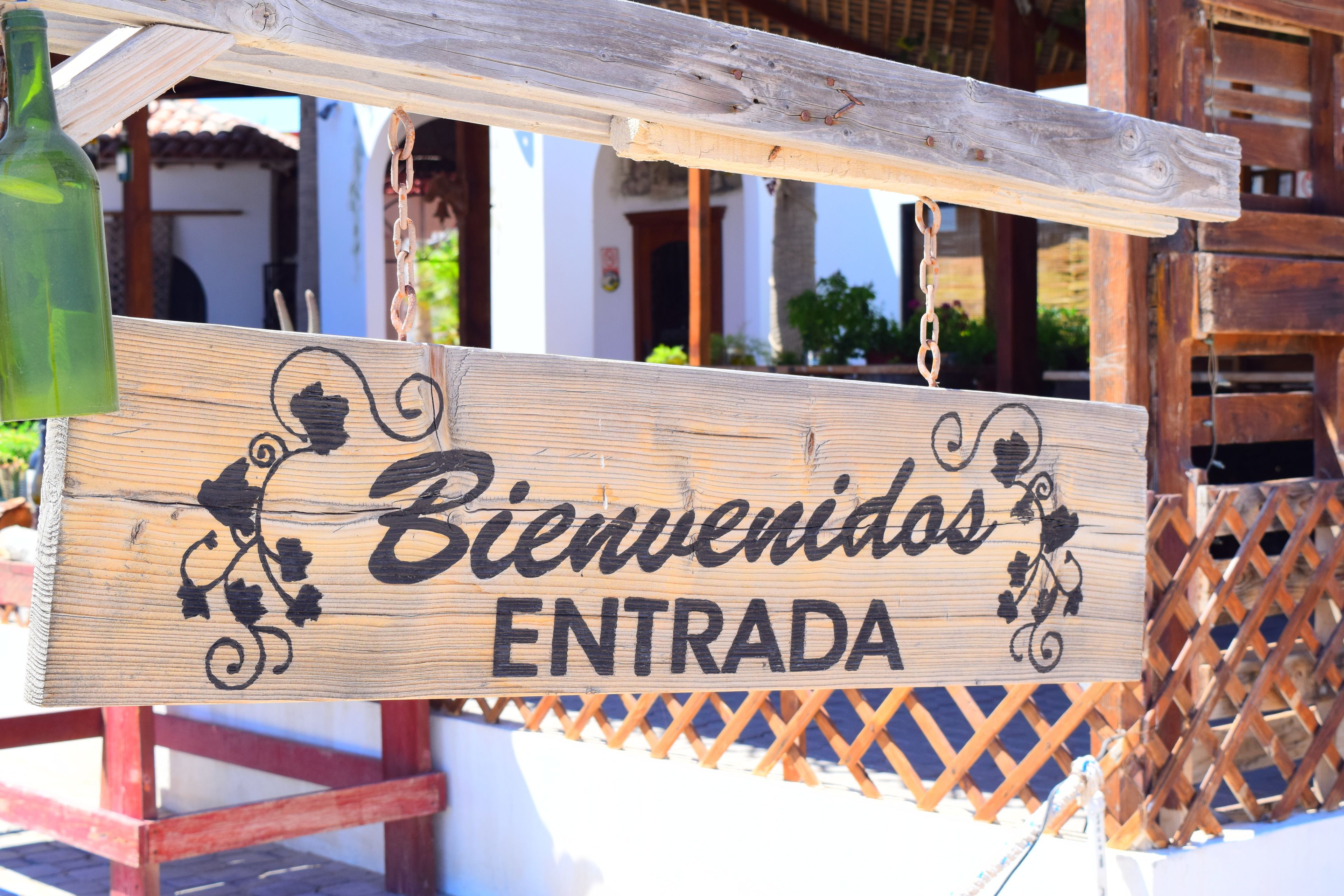 Een houten bord met de tekst 'Bienvenidos Entrada', hangend boven een houten hek.