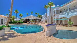 Un resort con dos piscinas, palmeras y una cabaña con techo de paja.