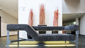 A modern, minimalist bench with metal legs and a grey cushioned seat in a spacious, well-lit lobby area. - Kyriad Vienna Altmannsdorf (Vienna)
