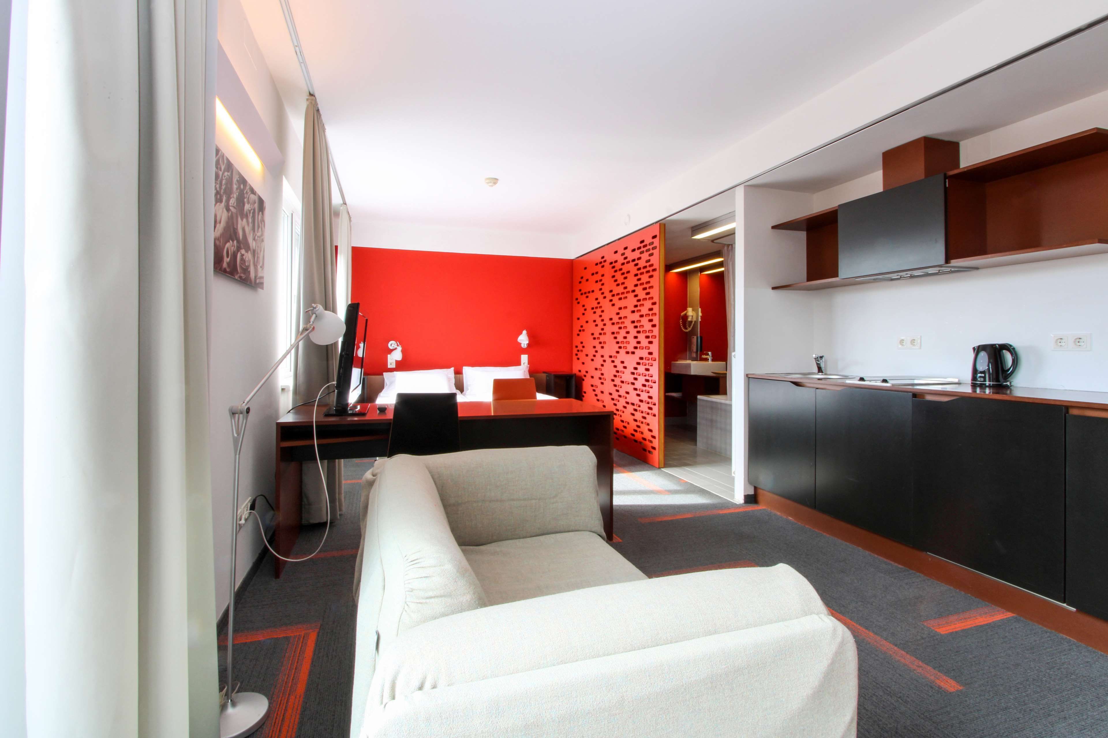 Una moderna camera d'albergo con angolo cottura, divano e una parete decorata di rosso.