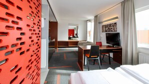A hotel room with a bed, a desk, a chair, a television, and a red decorative wall.