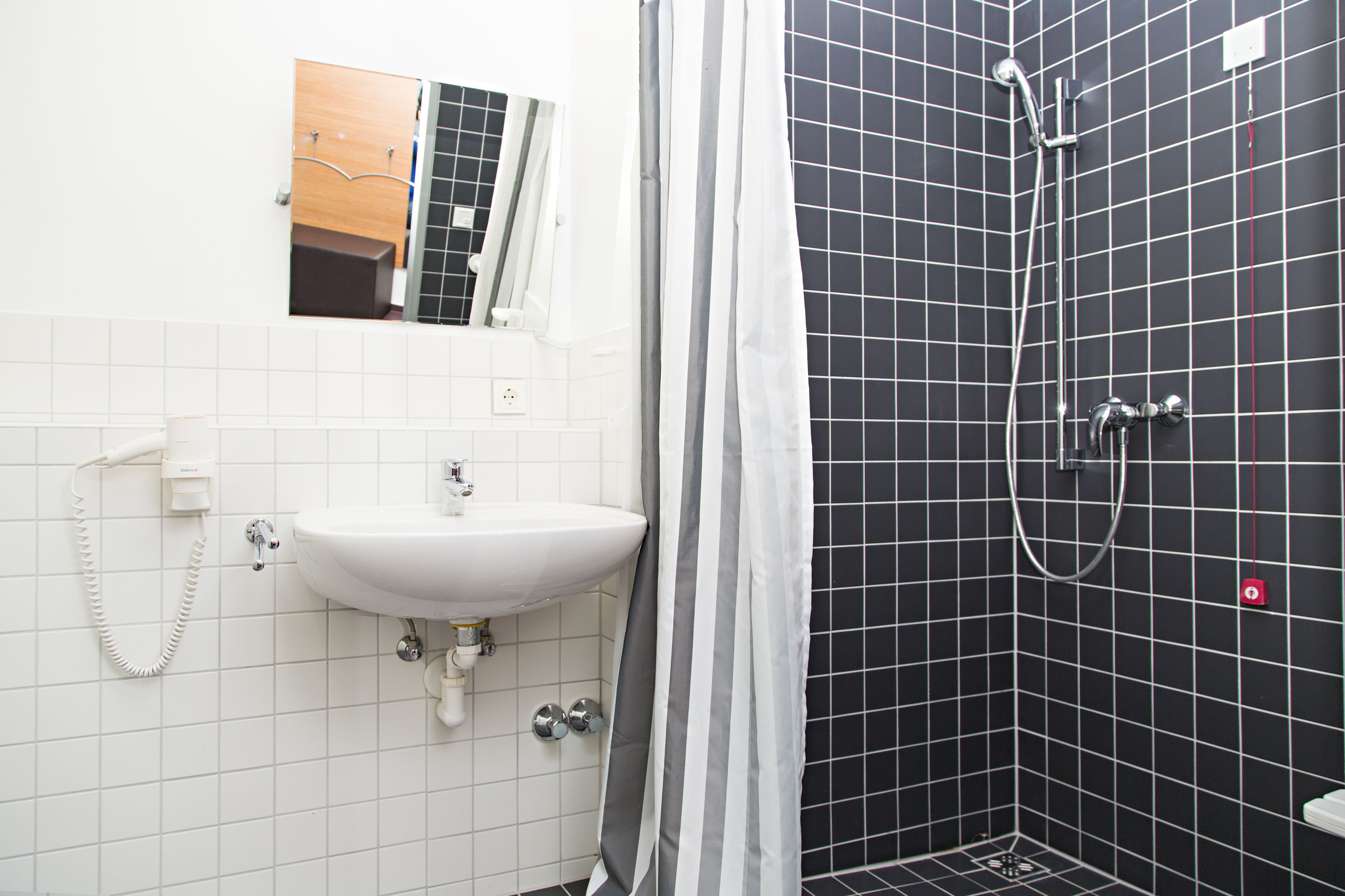 A bathroom with a white sink, a mirror, and a shower with black tiles.