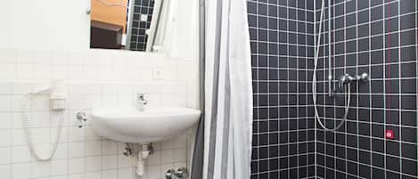 A bathroom with a white sink, a mirror, and a shower with black tiles.