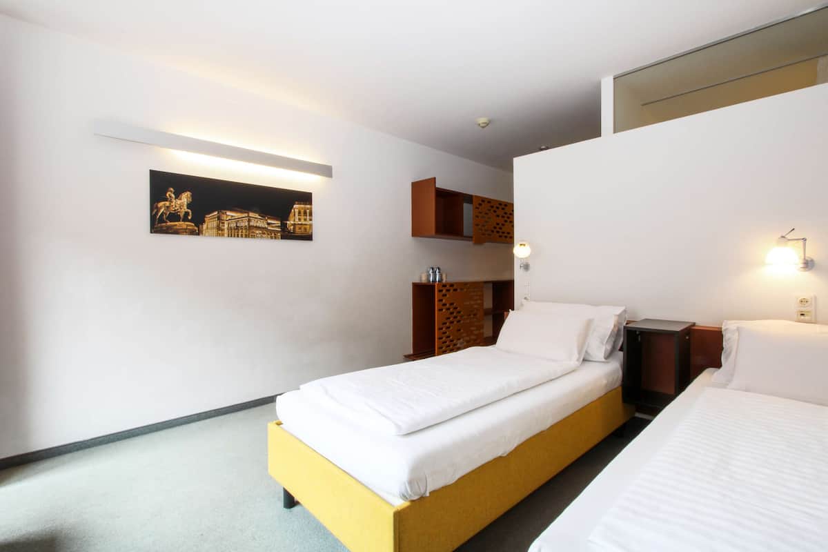 A hotel room with a bed, a nightstand, a wall-mounted shelf, and a framed picture.