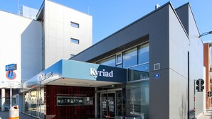 A modern hotel with a glass facade, a blue awning, and a sign reading "Kyriad." - Kyriad Vienna Altmannsdorf (Vienna)