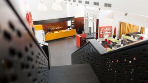 A modern hotel lobby with a central reception desk, seating area, and a staircase. - Kyriad Vienna Altmannsdorf (Vienna)