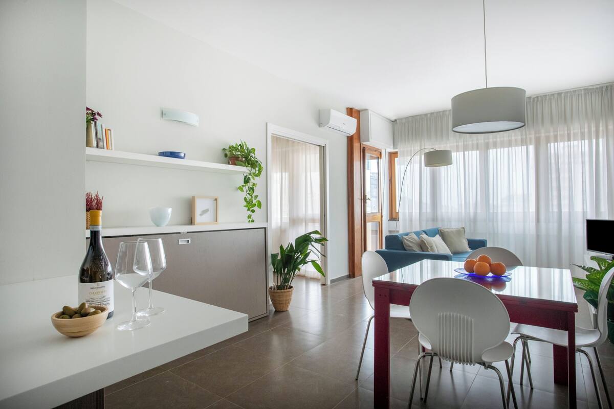 A modern living room with a dining area, a kitchen, and a TV.
