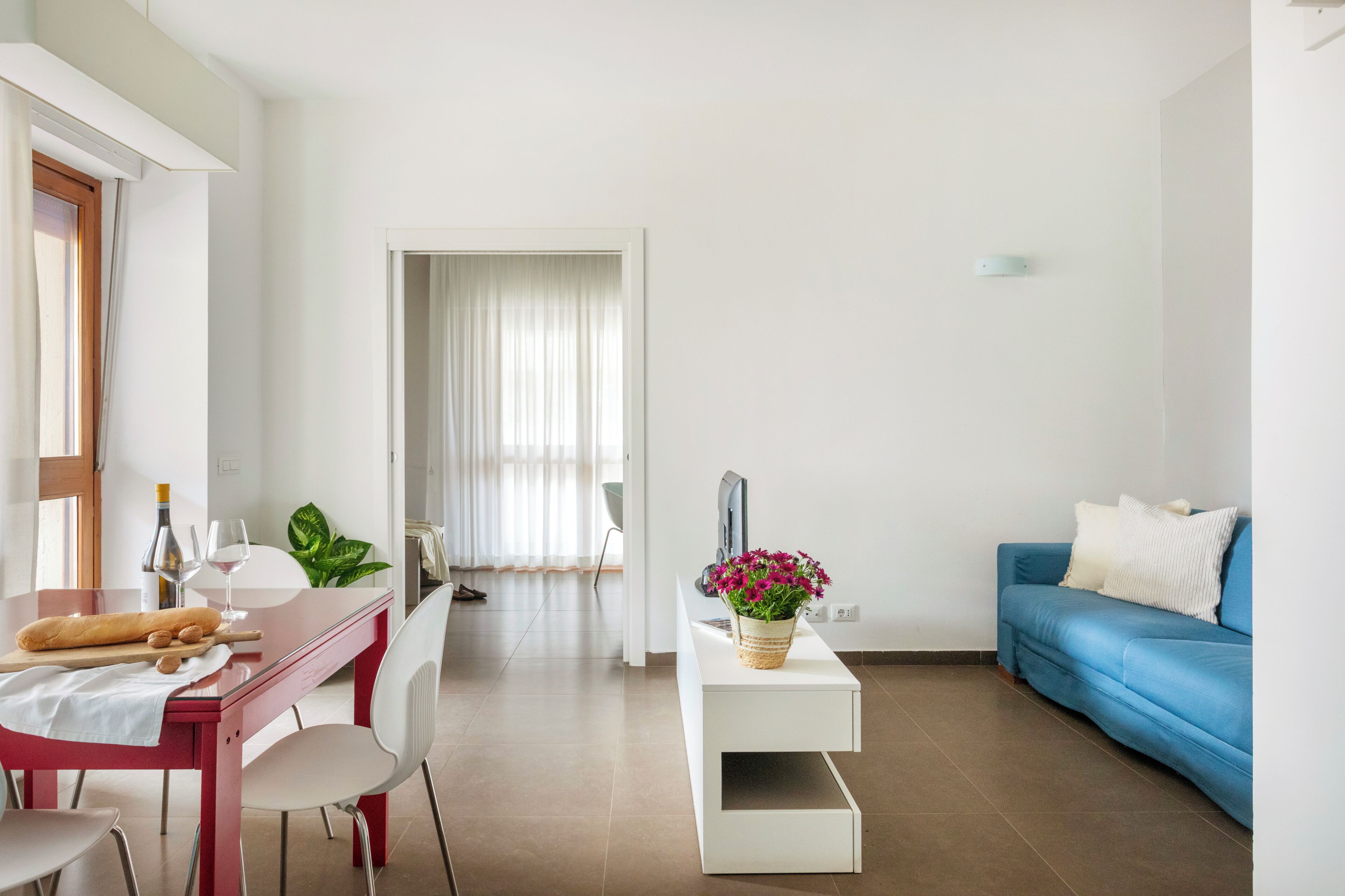 Una sala de estar moderna con comedor, un sofá azul, un televisor de pantalla plana y una planta en maceta.