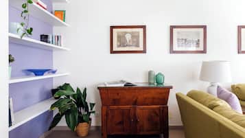 A room with a wooden cabinet, a green sofa, a white lamp, and shelves with books and decorative items.