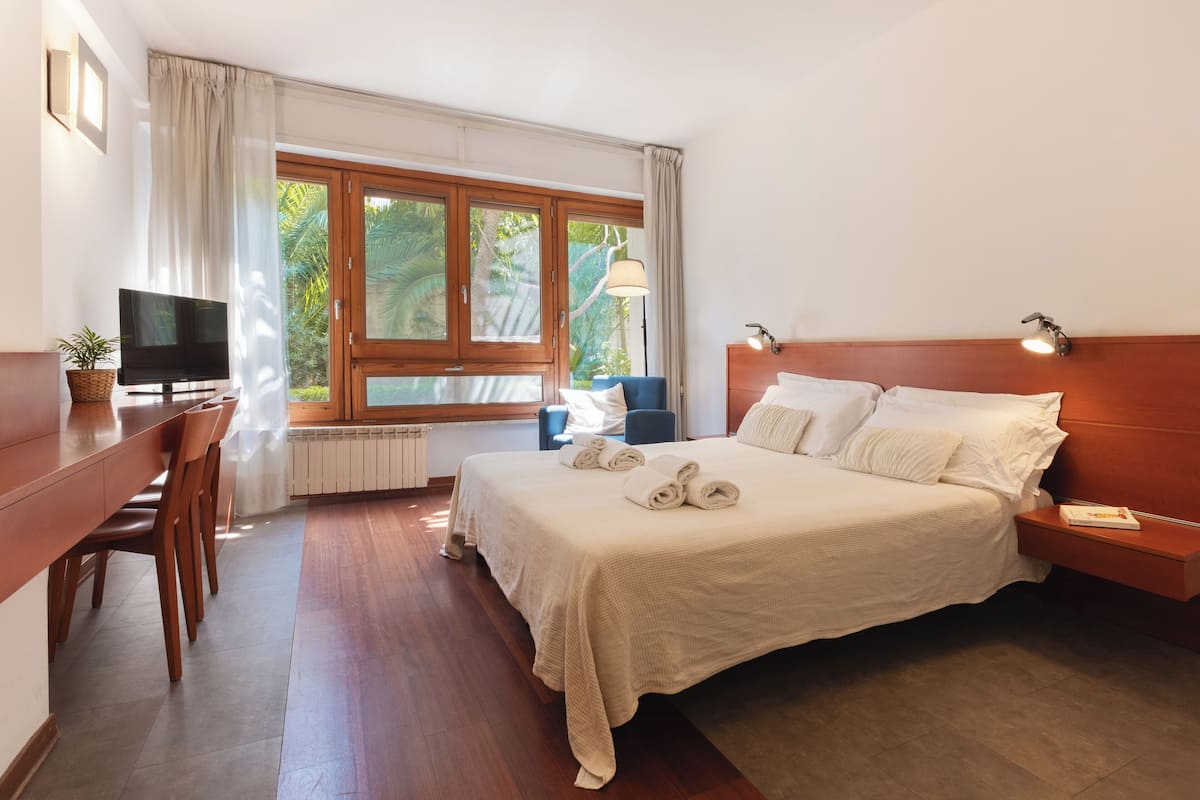A hotel room with a bed, a desk with a TV, a chair, a lamp, and a window with curtains.