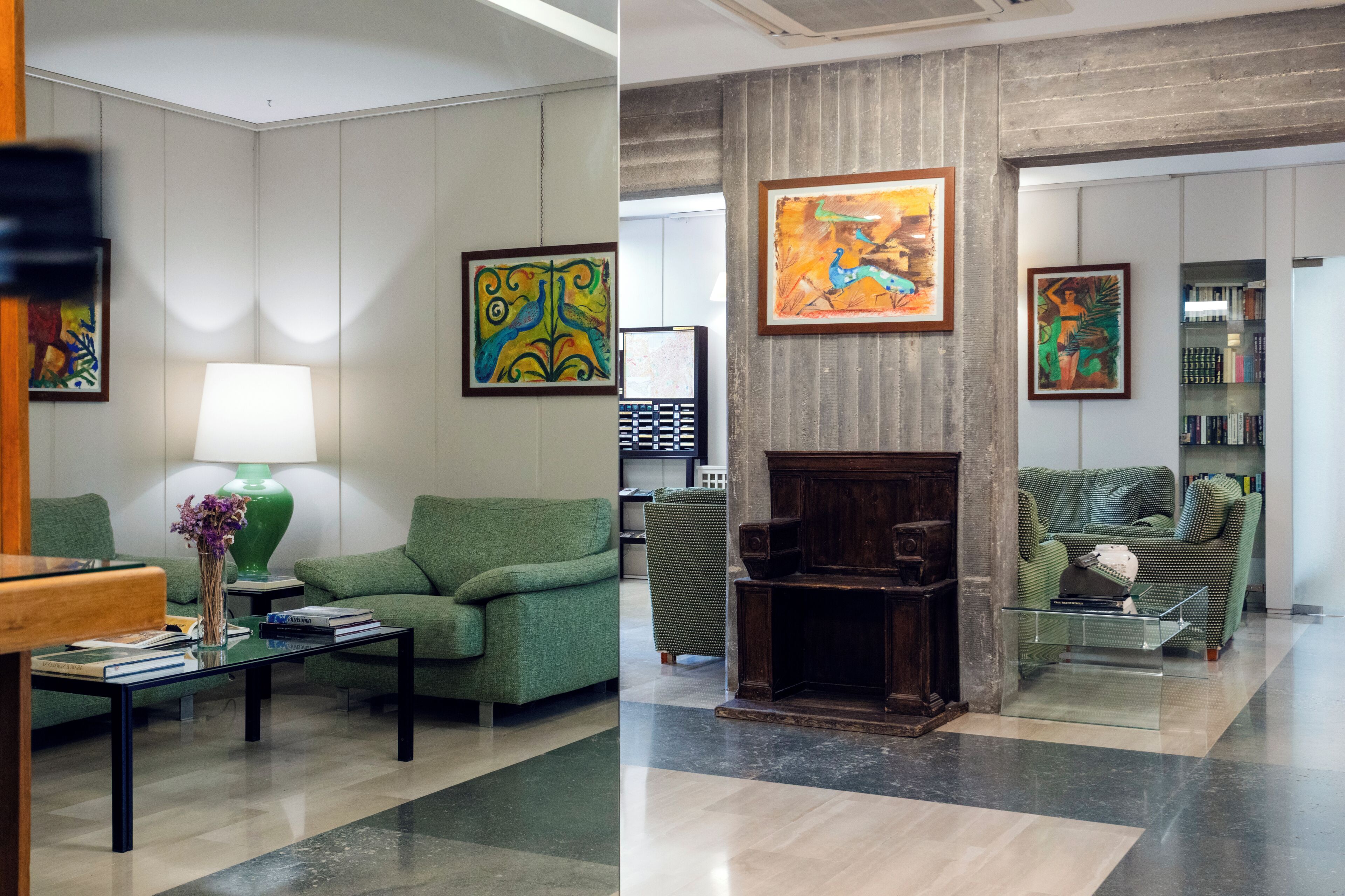 Eine Lobby mit grünen Sofas, einem Couchtisch, einer Lampe und Kunstwerken an den Wänden.