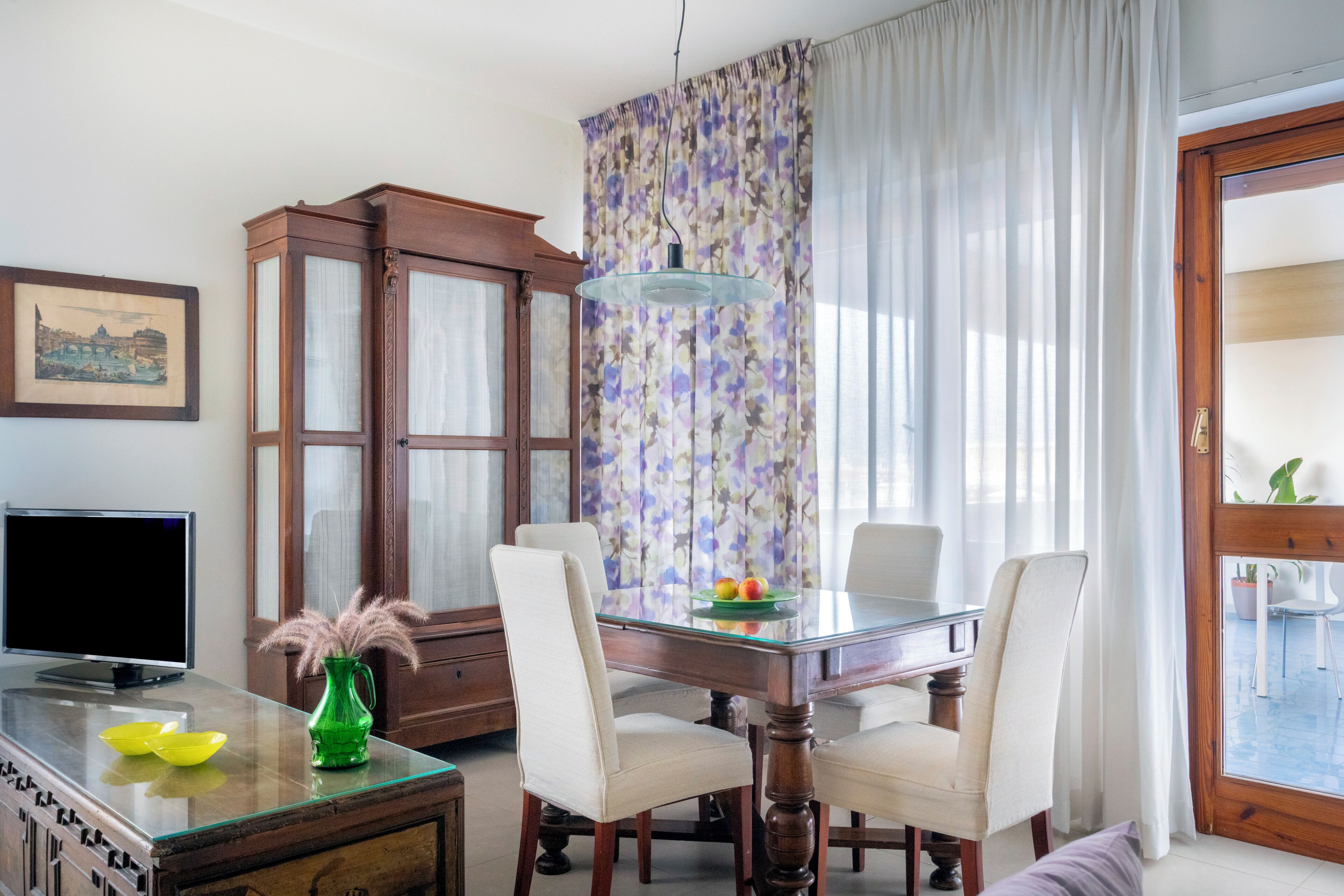 A dining area with a glass table, chairs, a cabinet, and a television.