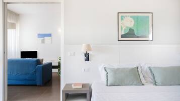 Una habitación de hotel con una cama, una mesita de noche, una lámpara, un sofá azul, un televisor y un cuadro en la pared.