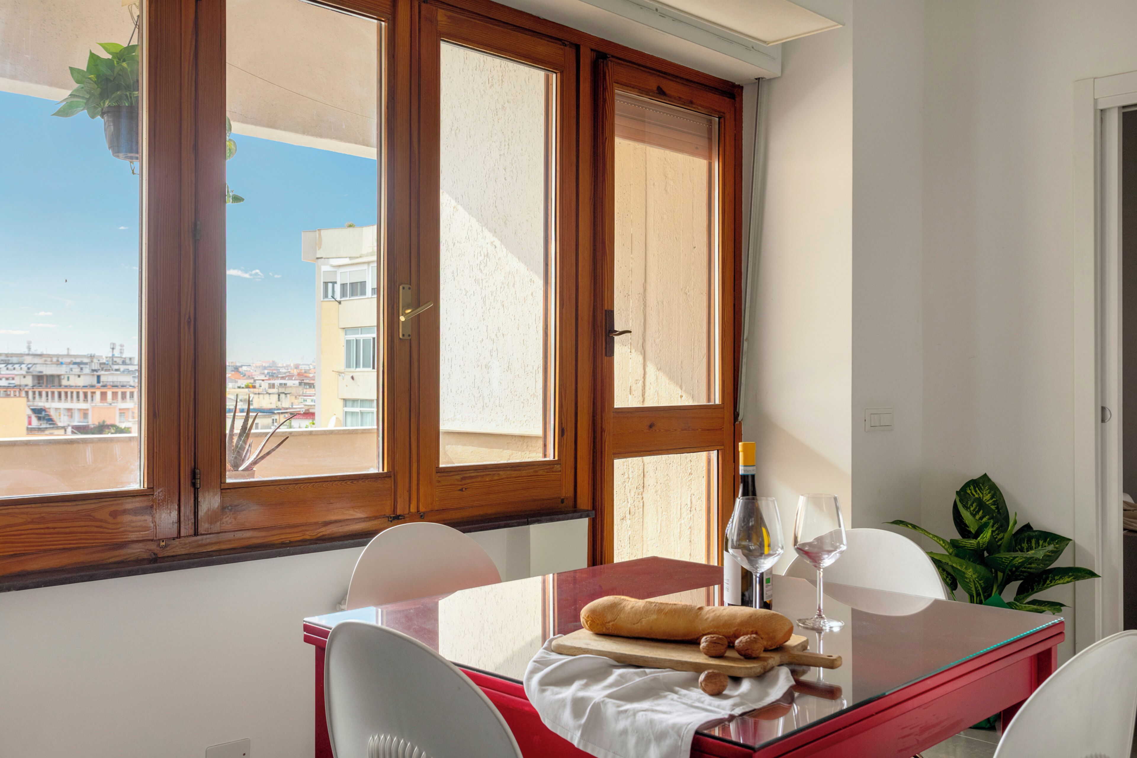 A dining area with a table, chairs, a bottle of wine, and a view through large windows.